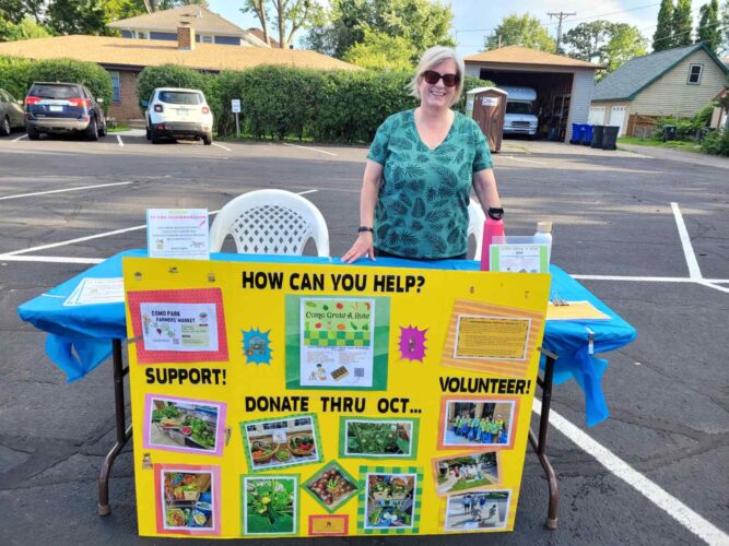 A volunteer smiles behind Como Park Lutheran Church’s community outreach table, featuring a colorful display about supporting, donating to, and volunteering with the Grow-a-Row program.