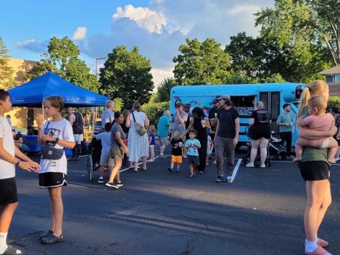Families and neighbors gather near a bright blue food truck and Saint Paul Parks and Recreation tent during an outdoor community event.